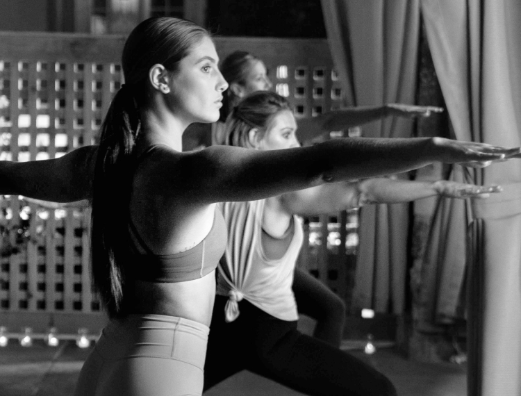 Yoga class full of women practicing warrior pose
