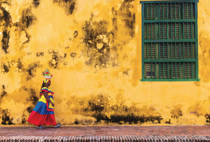 A woman walks with a fruit basket on her head
