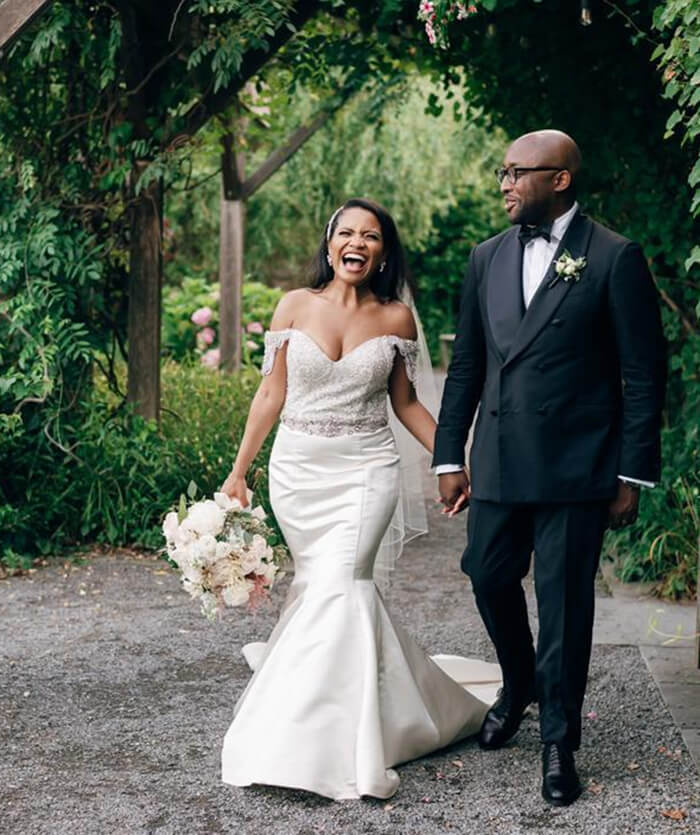 Bride laughing with groom while walking down a gravel path with greenery